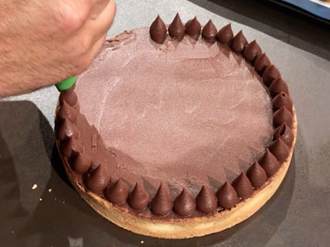 Une rangée de gouttes de ganache au chocolat est pochée sur tout le pourtour de la tarte