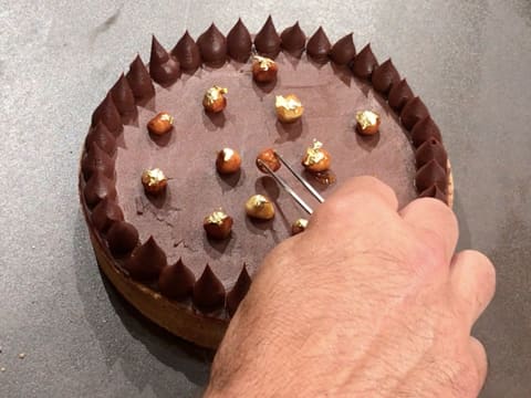 Les noisettes caramélisées sont déposées sur la tarte au chocolat avec une pince à dresser
