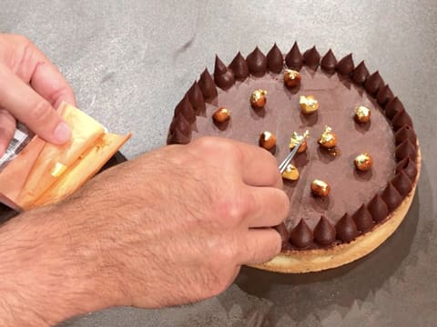 Un peu de feuille d'or est déposée sur les noisettes caramélisées qui sont sur la tarte au chocolat