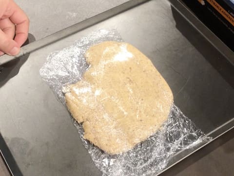 Obtention de la pâte sablée à la noix de pécan qui est enveloppée dans une feuille de papier film et posée sur une plaque à pâtisserie