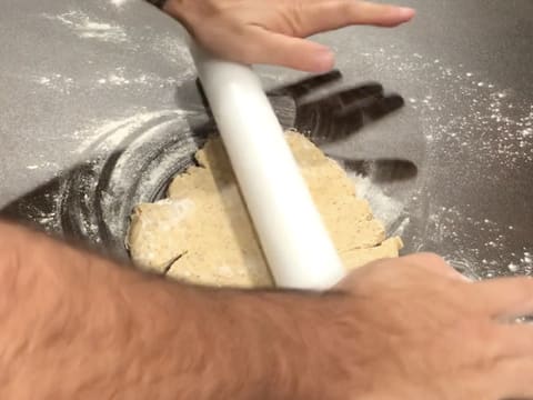 La pâte sablée à la noix de pécan est abaissée au rouleau à pâtisserie sur un plan de travail fariné