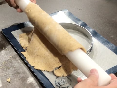 La pâte sablée à la noix de pécan est déroulée sur un cercle à tarte en inox qui est posé sur un tapis de cuisson en silicone