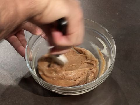 Incorporation du praliné noix de pécan dans la crème au chocolat blanc avec la spatule maryse dans le saladier en verre