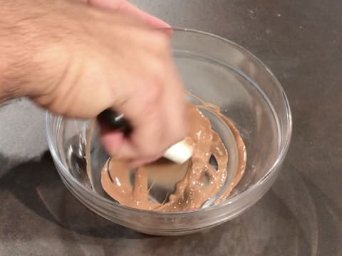 Mélange du chocolat au lait fondu dans un bol en verre, à l'aide de la spatule maryse