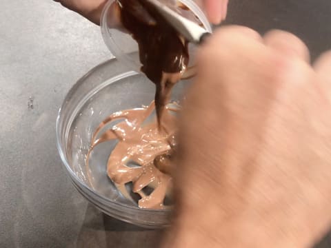 Ajout du praliné noix de pécan sur le chocolat au lait fondu dans le bol en verre posé sur le plan de travail