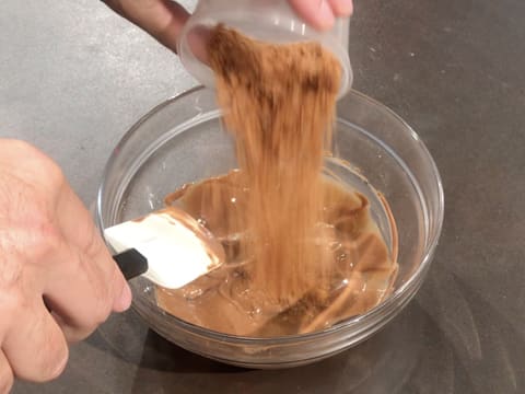 Ajout du pailleté feuilletine sur le chocolat au lait fondu et le praliné noix de pécan dans le bol en verre