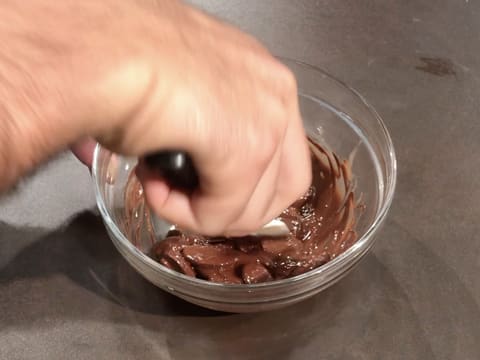 Mélange des fèves de chocolat noir partiellement fondues dans le bol en verre, à l'aide de le spatule maryse