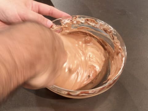 Mélange et obtention d'une préparation chocolatée lisse et homogène dans le grand bol en verre posé sur le plan de travail