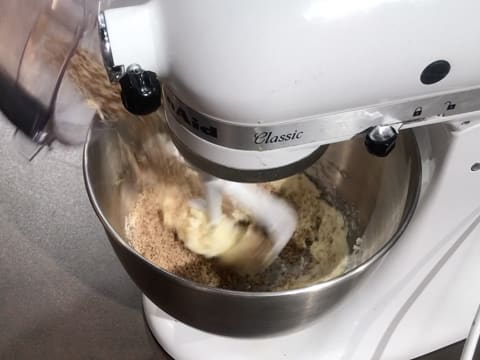 Ajout de la poudre de noix de pécan sur le beurre et le sucre glace crémés dans la cuve du batteur munie de l'accessoire feuille