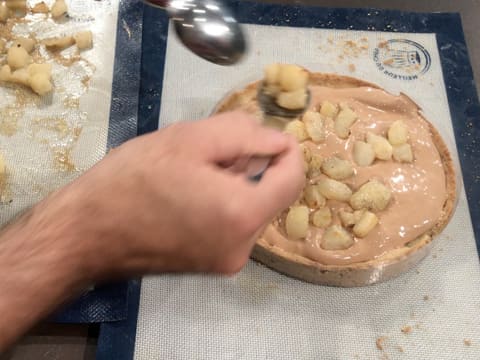 Des morceaux de poires rôties sont piqués sur toute la surface de la mousse qui est dans le fond de tarte sur le tapis de cuisson en silicone