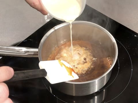 La crème liquide est versée sur le caramel, dans la casserole qui est sur la plaque de cuisson