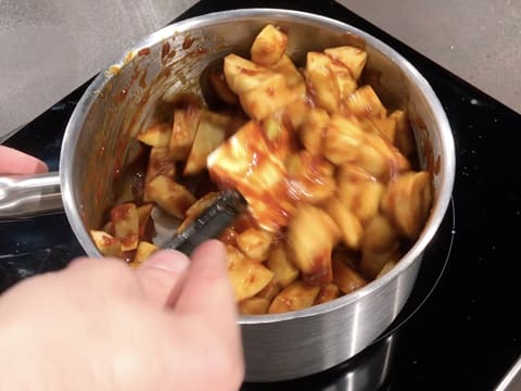 Les morceaux de pommes et le caramel sont mélangés ensemble avec la spatule maryse dans la casserole qui se trouve sur la plaque de cuisson