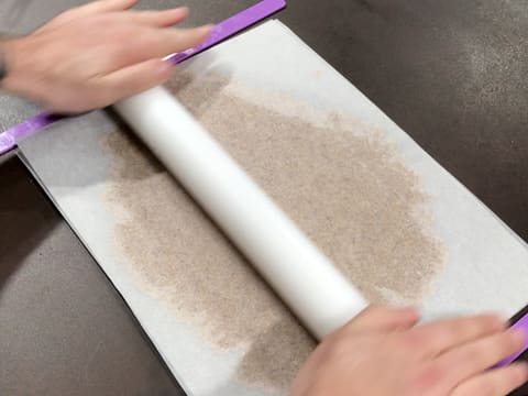 La pâte à streusel recouverte de la feuille de papier sulfurisé, est abaissée sur la largeur à l'aide d'un rouleau à pâtisserie et de deux réglettes à niveler positionnées de chaque côté de la pâte