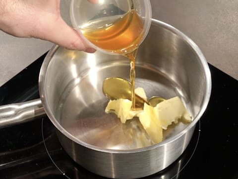 Du miel est versé dans une casserole qui contient du beurre et qui est placée sur une plaque de cuisson