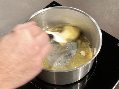 Le beurre et le miel sont en train de fondre dans la casserole, tout en étant mélangés avec une spatule type maryse