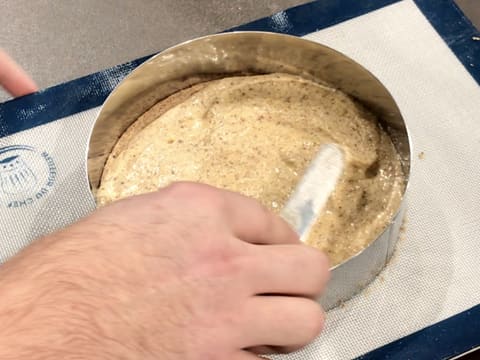 La préparation de moelleux aux noisettes qui est dans le cercle à mousse, est lissée à l'aide d'une petite spatule métallique coudée