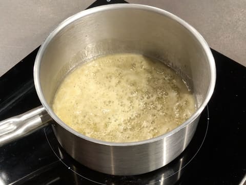 Le beurre et le miel fondus sont en train de cuire dans la casserole qui est posée sur la plaque de cuisson