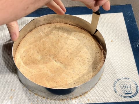 La lame d'un couteau est passée entre le cercle à mousse et le biscuit qui sont posés sur le tapis de cuisson silicone