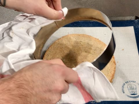 Le cercle à mousse est retiré à l'aide d'un torchon et le disque de biscuit reste posé sur le tapis de cuisson en silicone