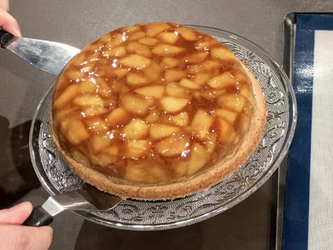 La tarte tatin revisitée aux pommes est placée sur son plat de service à l'aide de deux spatules métalliques coudées