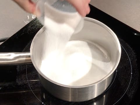 Du sucre en poudre est versé dans une casserole qui est placée sur une plaque de cuisson