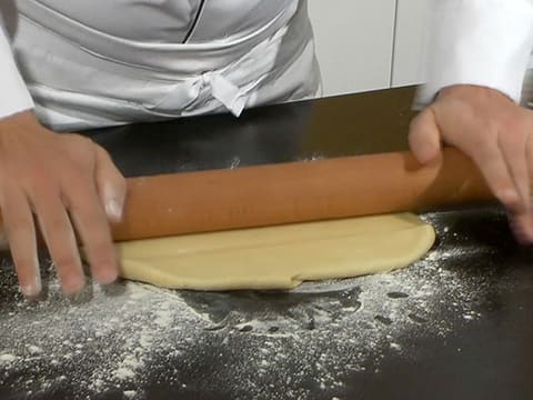 La pâte brisée est étalée au rouleau à pâtisserie sur le plan de travail fleuré