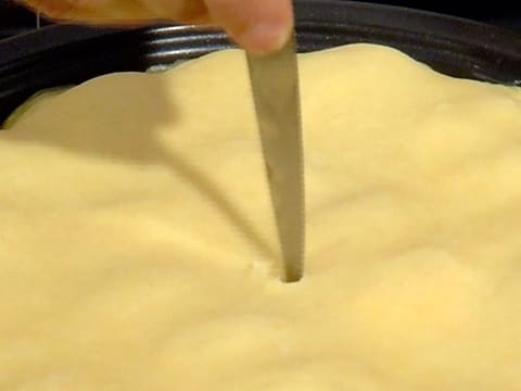 Un trou est formé avec la pointe d'un couteau pour faire une cheminée au milieu de la pâte brisée qui est posée sur les pommes dans le moule à tarte tatin