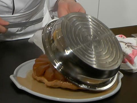 Le moule à tarte tatin est soulevé pour laisser apparaître la tarte tatin qui est sur l'assiette de présentation