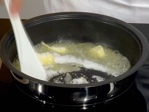 Le sucre en poudre et le beurre qui est en train de fondre dans le moule à tarte tatin sont mélangés ensemble à l'aide de la spatule