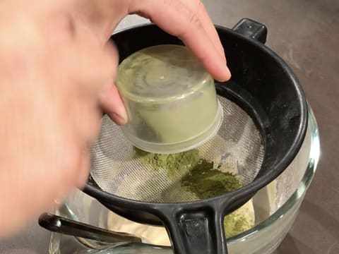 Le thé matcha en poudre est tamisé dans la passoire tamis qui est posée sur la cuve du batteur qui contient la préparation à l'amande
