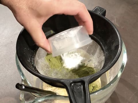 La farine est tamisée avec le thé matcha en poudre dans la passoire tamis qui est posée sur la cuve du batteur qui contient la préparation à l'amande