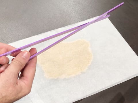 La pâte à streusel amande est recouverte d'une feuille de papier sulfurisé et deux réglettes à niveler violettes sont au premier plan