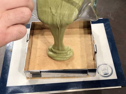 La pâte à biscuit thé matcha est versée sur le biscuit streusel amande qui est dans le cadre inox posé sur une plaque à pâtisserie recouverte d'un tapis de cuisson en silicone