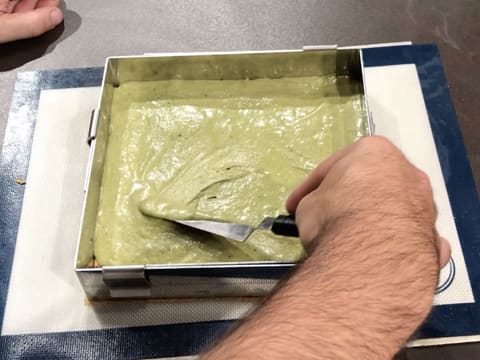 La pâte à biscuit thé matcha est étalée avec une petite spatule métallique coudée sur toute la surface du biscuit streusel amande qui est dans le cadre inox posé sur un tapis de cuisson en silicone