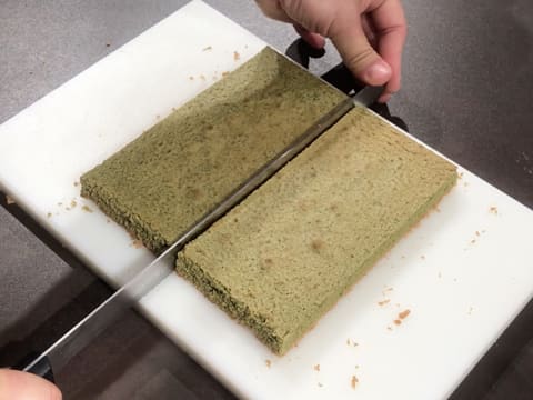 Le biscuit thé matcha est coupé en son milieu avec le couteau-scie à génoise sur la planche à découper