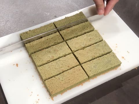Le biscuit thé matcha est coupé en dix rectangles avec le couteau-scie à génoise sur la planche à découper