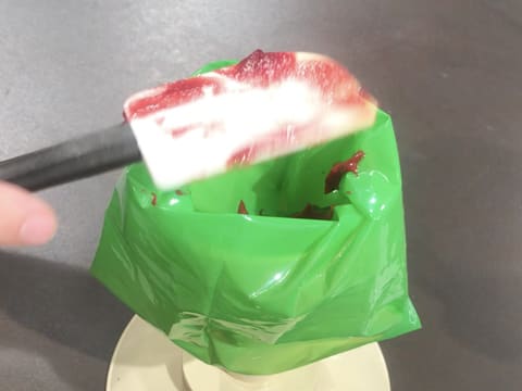 Le confit de framboise est placé dans une poche pâtissière qui est posée sur un support poche à douille sur le plan de travail