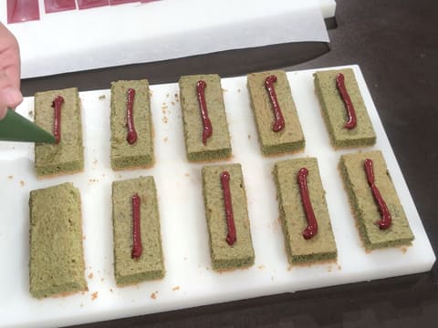 Un cordon de confit de framboise est poché sur le milieu des rectangles de biscuit thé matcha qui sont posés sur la planche à découper