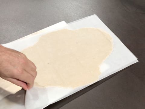 La pâte à streusel amande entourée de ses deux feuilles de papier sulfurisé, est glissée sur une plaque à pâtisserie