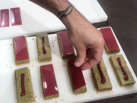 Les plaquettes en chocolat inspiration framboise sont déposées sur les rectangles de biscuit thé matcha qui sont posés sur la planche à découper