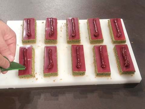 Un cordon de confit de framboise est poché au milieu des plaquettes en chocolat inspiration framboise qui sont sur les rectangles de biscuit thé matcha