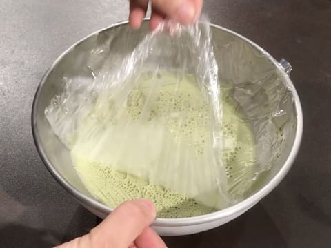 La feuille de papier film est retirée du dessus du crémeux matcha chocolat blanc qui se trouve dans le cul de poule sur le plan de travail