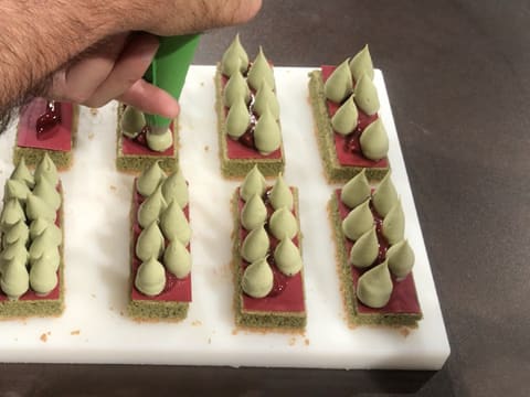 Des gouttes de crémeux matcha chocolat blanc sont pochées à la poche à douille sur les rectangles de biscuit thé matcha recouverts des plaquettes en chocolat inspiration framboise