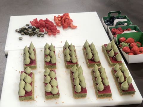 Obtention des tartelettes thé matcha et des fruits rouges taillés en petits morceaux, le tout sur la planche à découper posée sur le plan de travail