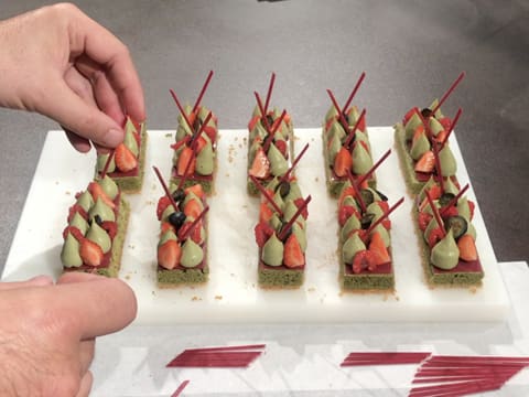 Les petits bâtonnets en chocolat inspiration framboise sont piqués dans le crémeux matcha chocolat blanc sur les tartelettes aux fruits rouges et thé matcha