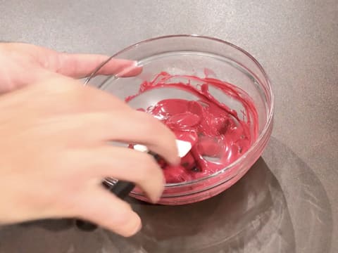 Mélange du chocolat inspiration framboise fondu dans le bol en verre, à l'aide d'une spatule type maryse