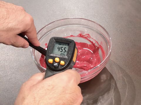 Prise de la température du chocolat inspiration framboise dans le bol en verre, à l'aide d'un thermomètre à visée laser qui affiche 45,5°C