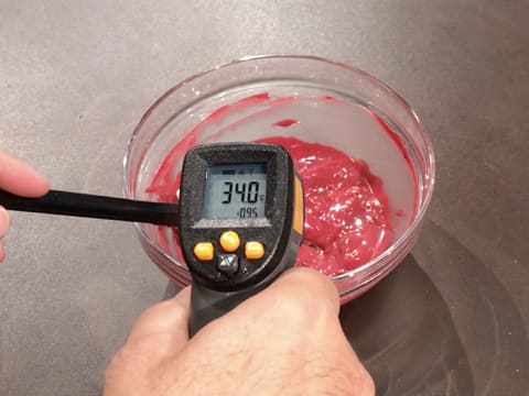 Prise de la température du chocolat inspiration framboise dans le bol en verre, à l'aide d'un thermomètre à visée laser qui affiche 34,0°C