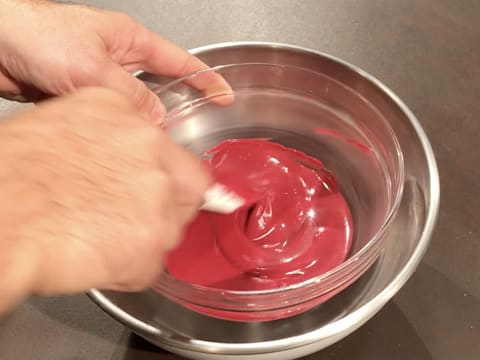 Mélange à la spatule maryse du chocolat inspiration framboise dans le bol en verre qui trempe dans un cul de poule rempli d'eau