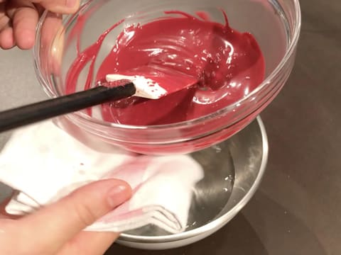 Le bol en verre qui contient le chocolat inspiration framboise fondu est essuyé par le dessous avec un torchon